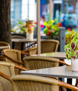 An outdoor café with wicker chairs and tables, adorned with colorful potted plants, creating a vibrant and inviting atmosphere.