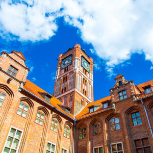 A brick building with a tall clock tower rises against a blue sky dotted with clouds, showcasing architectural details.